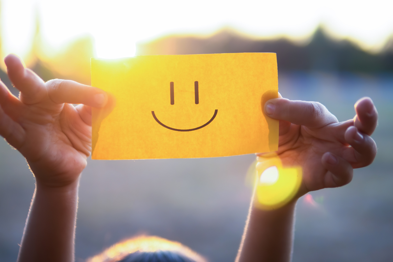 A person holding up a card with a smiley face on it.